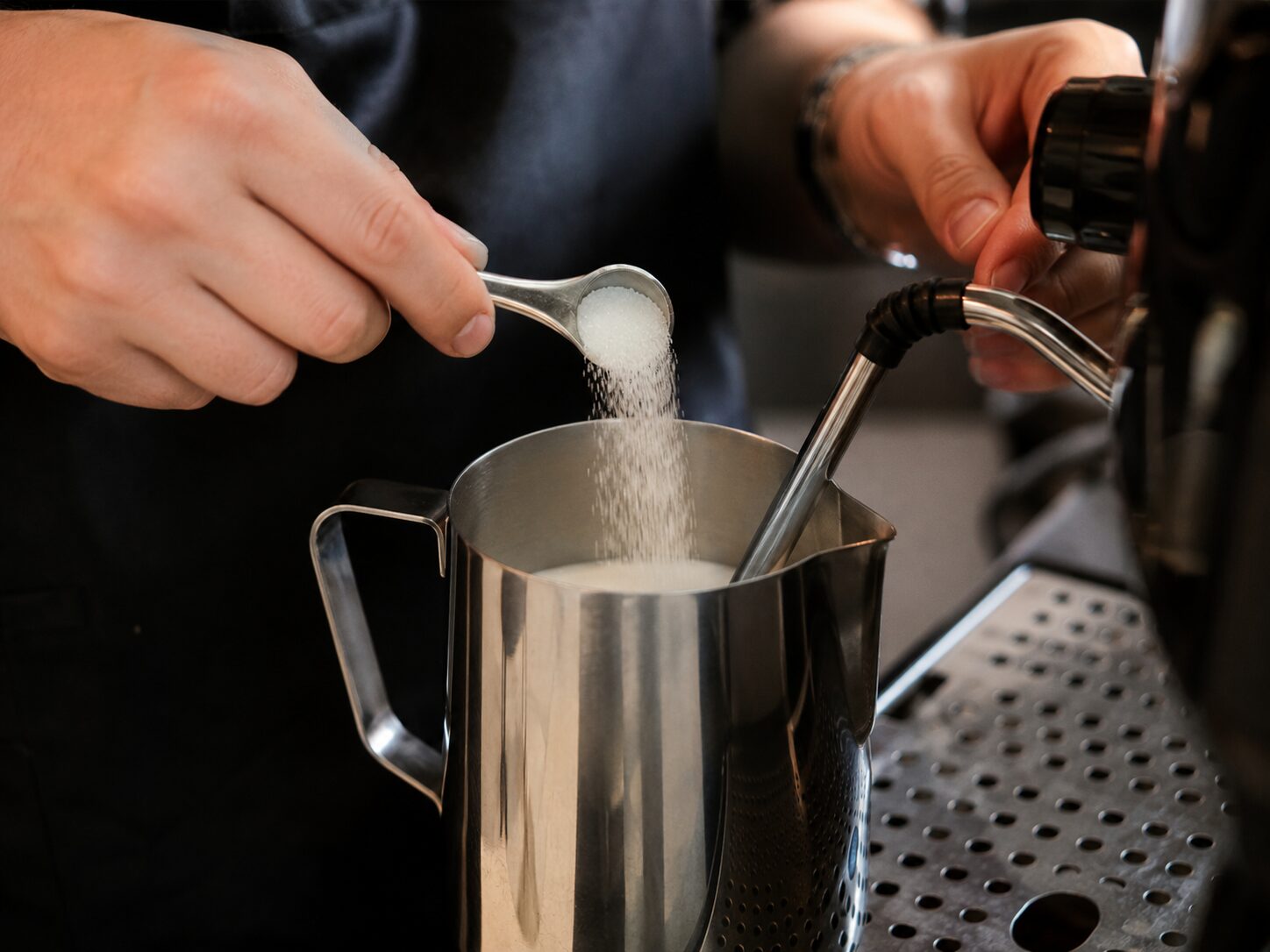 Barista adding sugar to milk before steaming for a sweet latte
