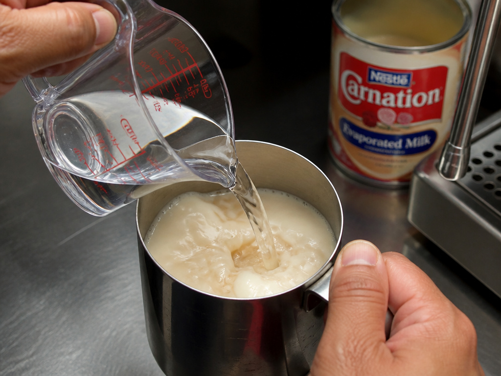 Mixing evaporated milk with water in a pitcher before steaming for coffee.