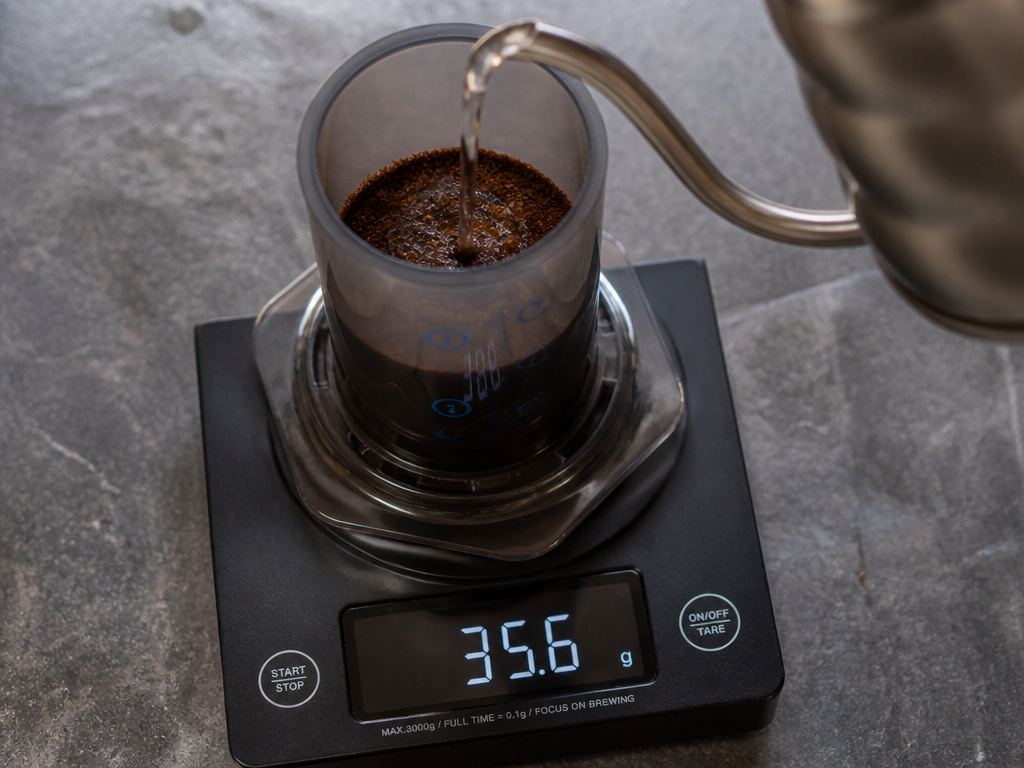 Precision scale measuring coffee and water for brewing ratio calculation.