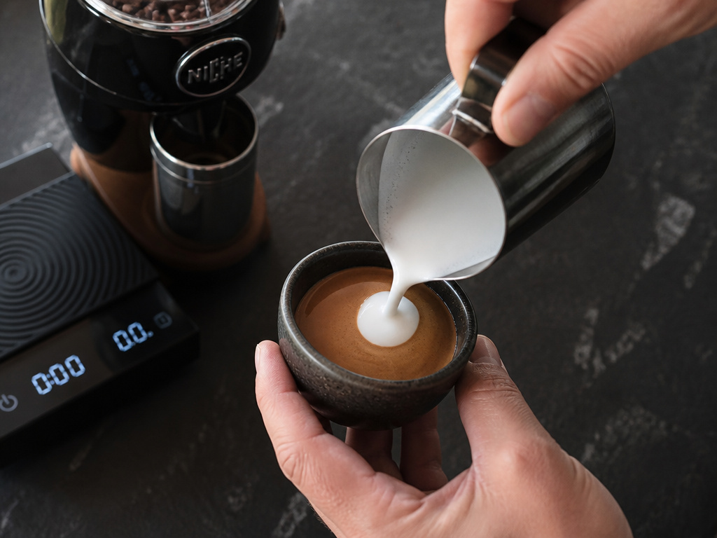 Close-up of hands preparing a traditional espresso macchiato at home.