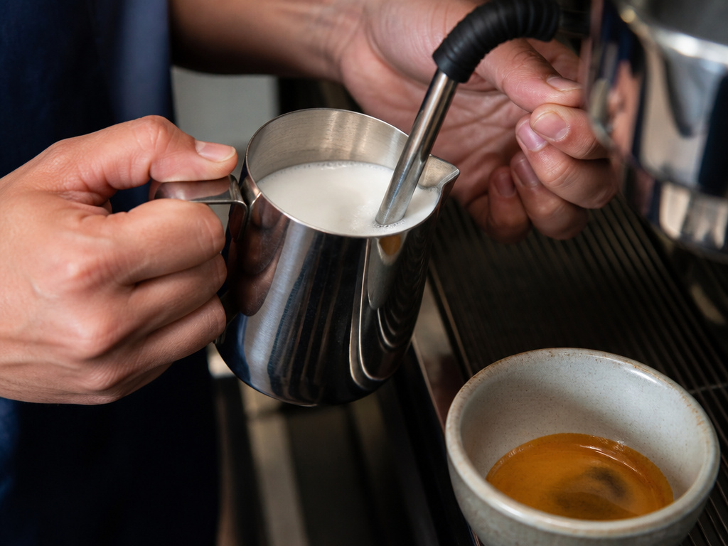 Barista steaming milk for a latte beside a fresh espresso shot.