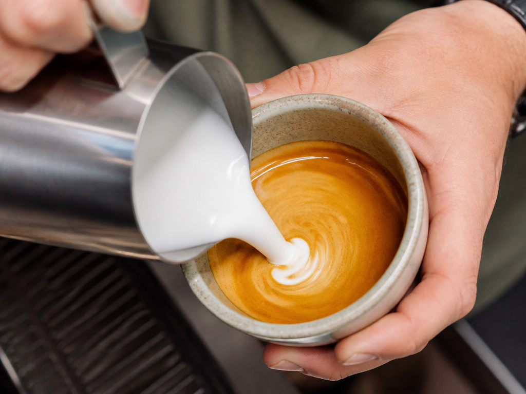 Pouring steamed milk into espresso to make a homemade latte.